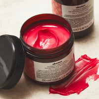 Thumbnail for Open jar of red hair product with a bottle in the background on a light surface