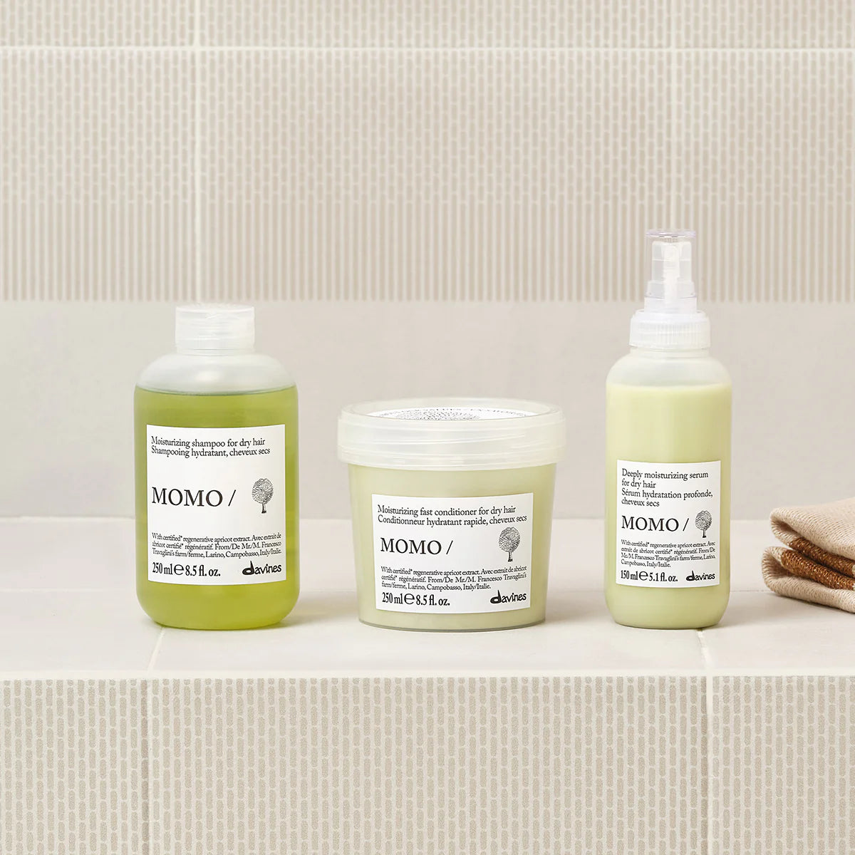 Three Momo hair care products on a bathroom counter with a tiled wall background.