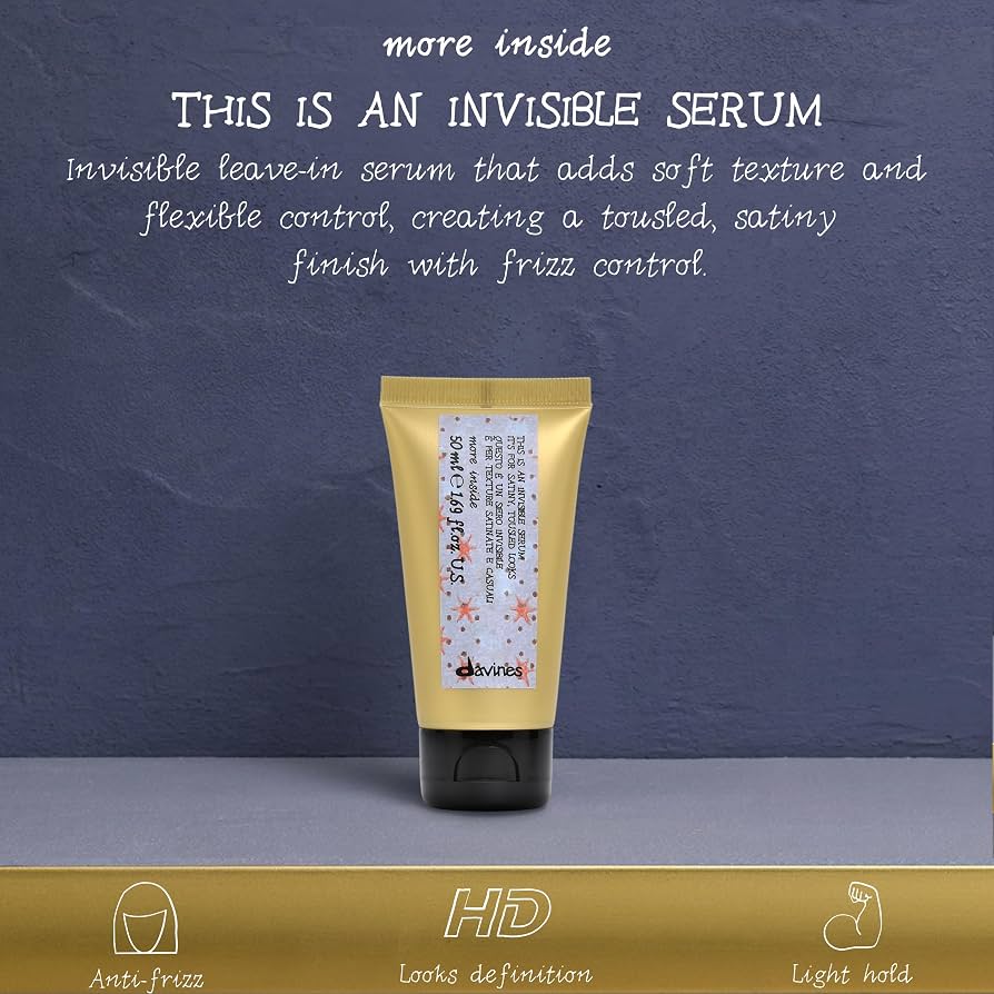 A squeeze tube of hair serum with a pale yellow body and black cap, standing upright against a textured dark blue-gray background. White text at the top reads 'THIS IS AN INVISIBLE SERUM' with descriptive copy about adding soft texture and frizz control.