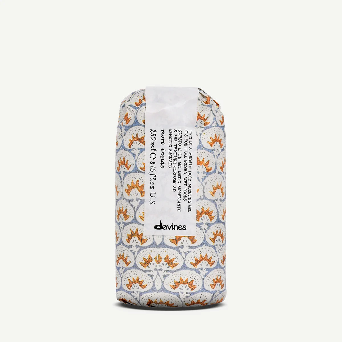 Davines Wette Celand 250ml roll-on bottle with a patterned paper sleeve featuring orange and white floral motifs on a light gray background, set against a plain off-white studio backdrop.