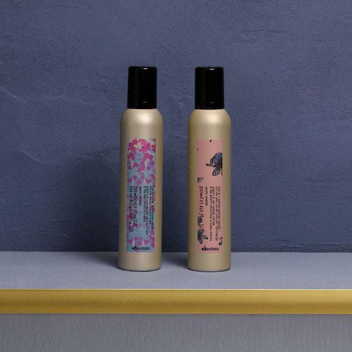 Two gold hair care products with black caps on a gray surface against a blue wall.
