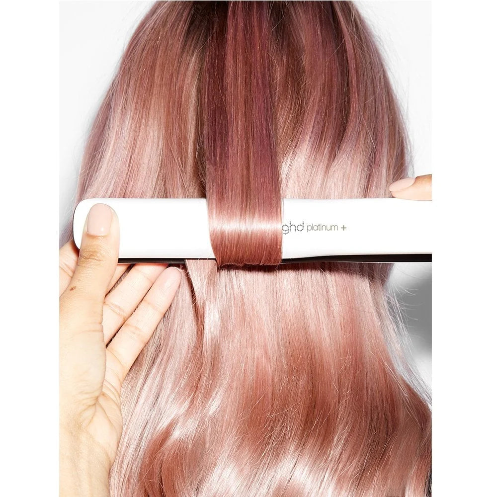 Person using a ghd hair straightener on pink hair against a white background