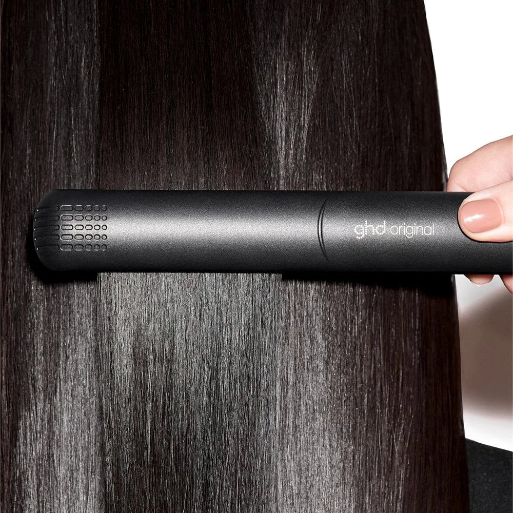Person using a ghd hair straightener on dark hair