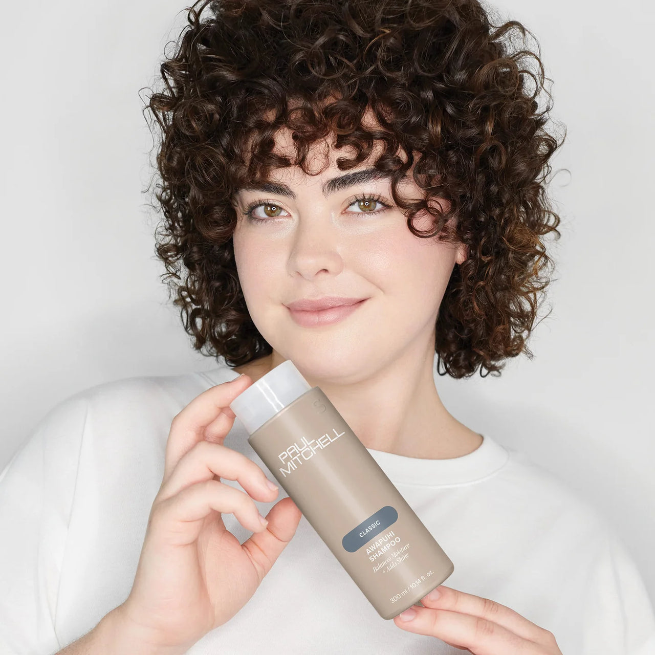 Person holding a bottle of Paul Mitchel shampoo against a plain background