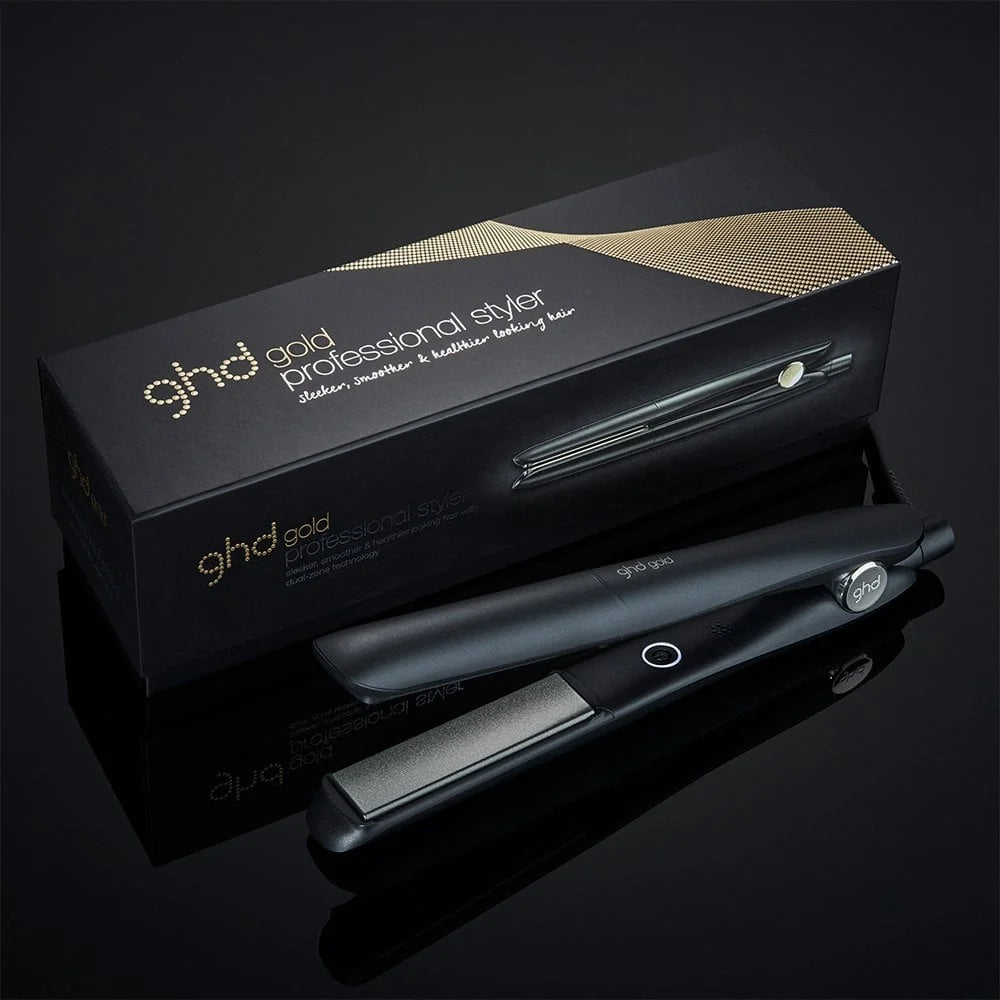 A black ghd gold Professional Styler hair straightener shown next to its black and gold retail box on a reflective black surface.