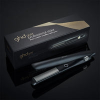 Thumbnail for A black ghd gold Professional Styler hair straightener shown next to its black and gold retail box on a reflective black surface.