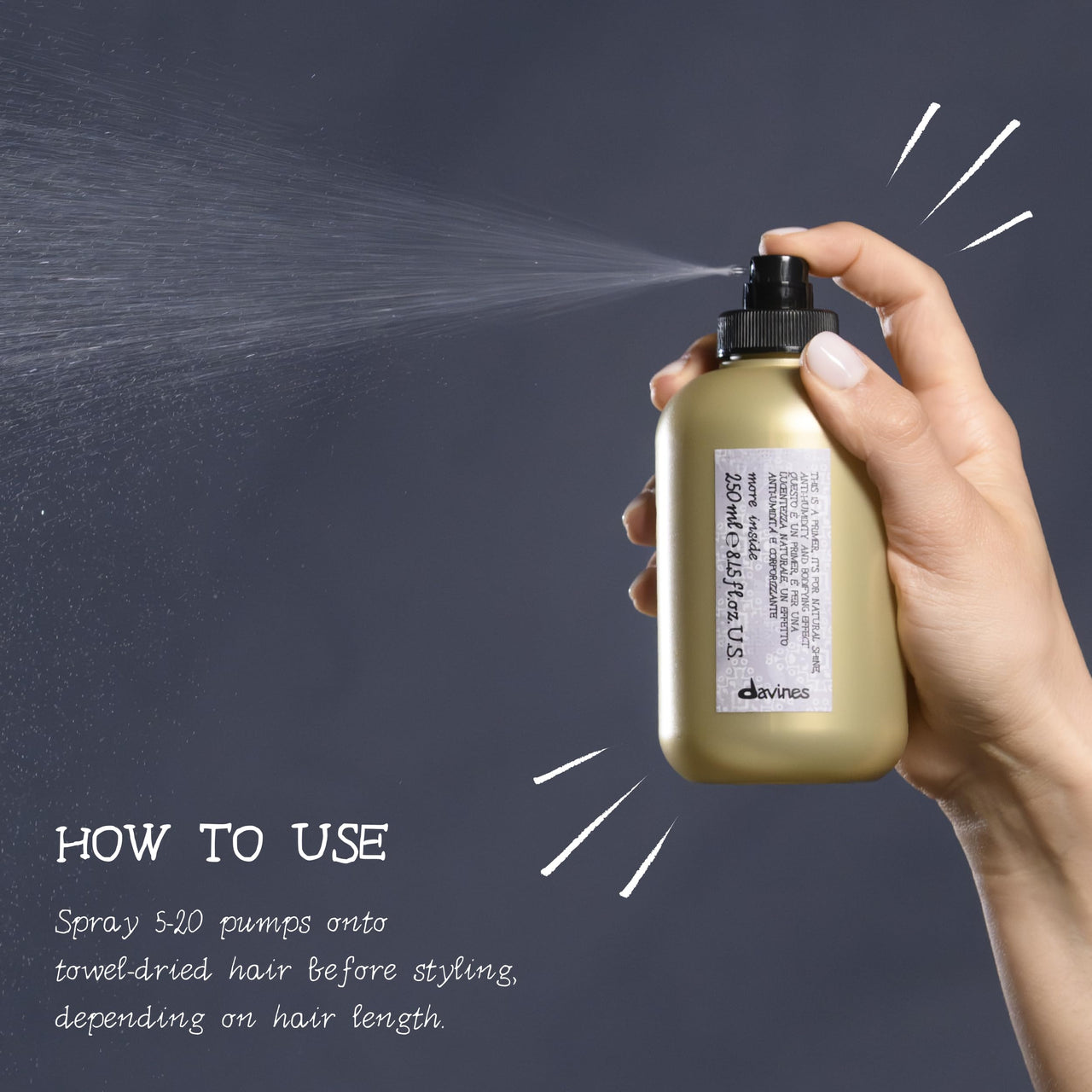 A hand holding a Devines gold spray bottle that is spraying mist, with text on the left explaining how to use the product on towel-dried hair.