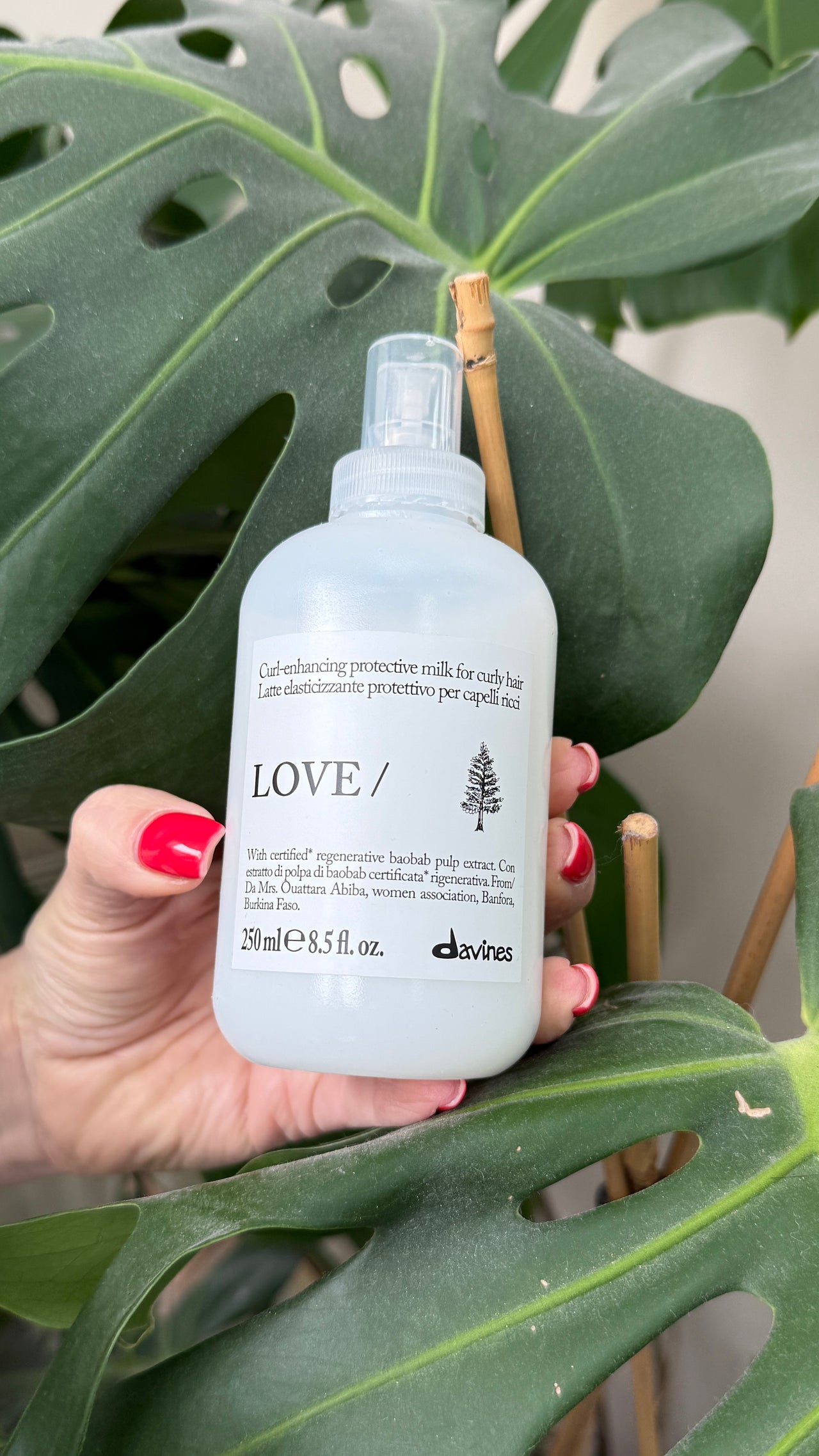 Hand holding a Davines hair care product bottle against a leafy background