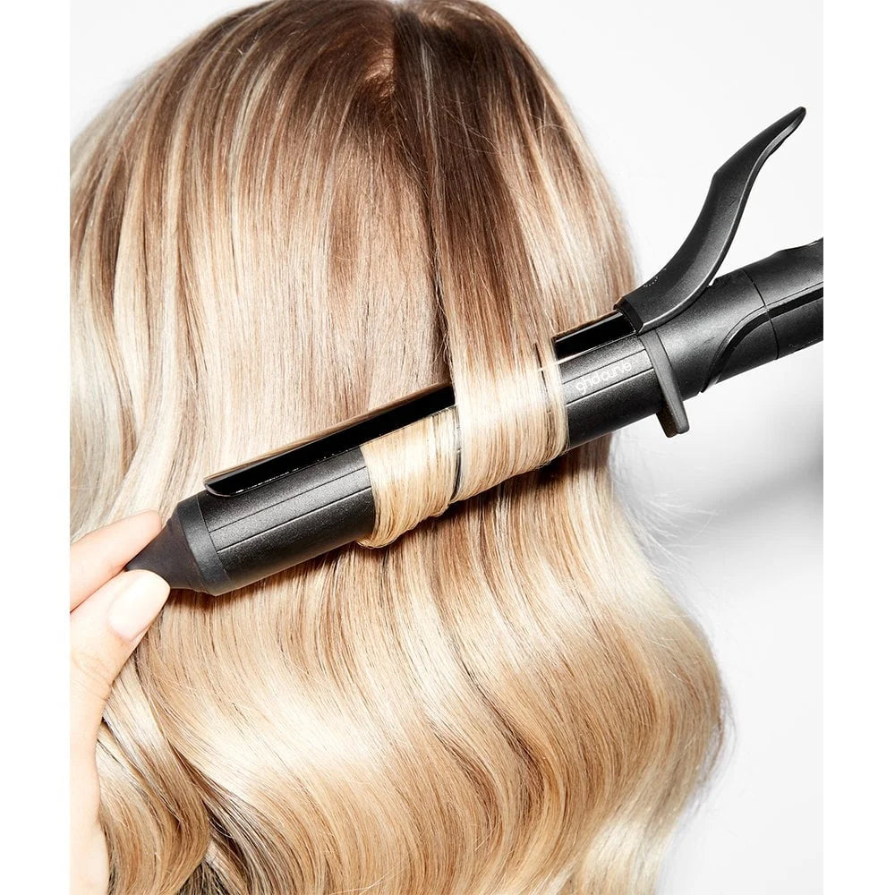 Person using a hair curling iron on blonde hair against a white background