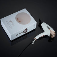 Thumbnail for A white and rose gold hair dryer shown next to its white retail box on a glossy black reflective surface. The box features the brand name 'ghd' and 'Hair Pro'.