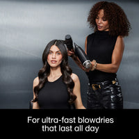Thumbnail for Woman getting her hair styled by another woman with a hair dryer against a gray background.