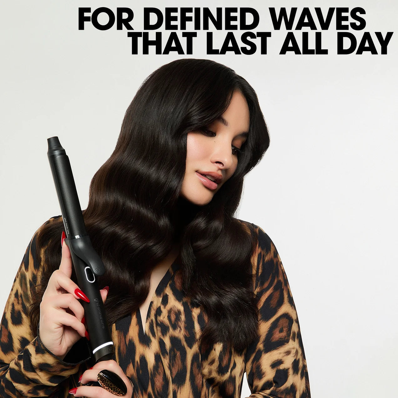 Woman with styled hair holding a curling iron against a light background