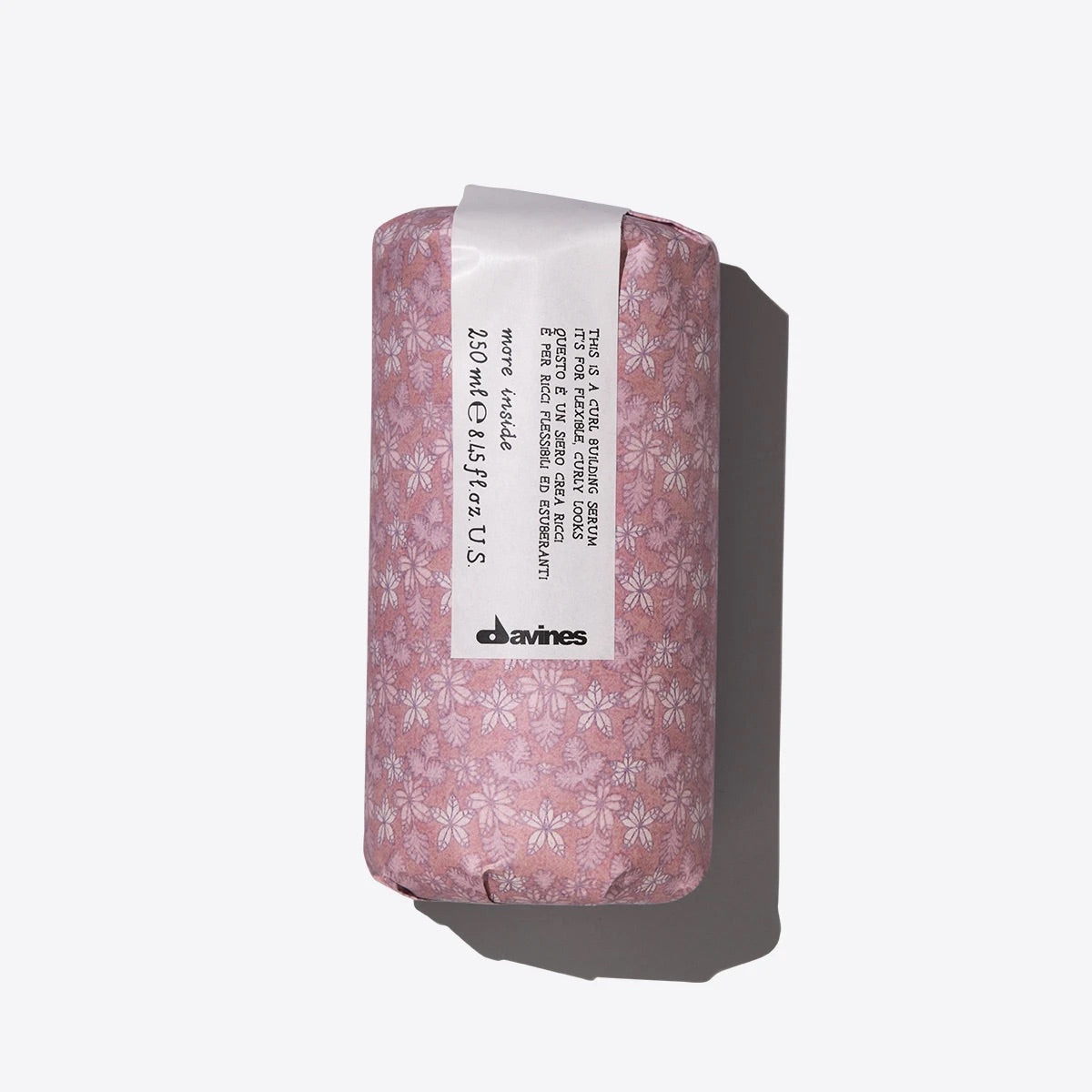 A bottle of Davines This is a Curl Building Serum Curl Enhancing Hair Serum with a pink label and a floral pattern.